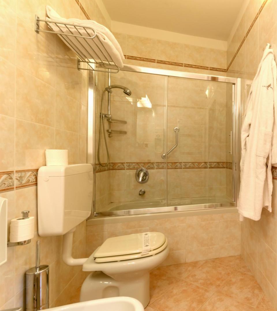 Badezimmer mit Glasdusche, WC, Handtuchhalter und Haken.