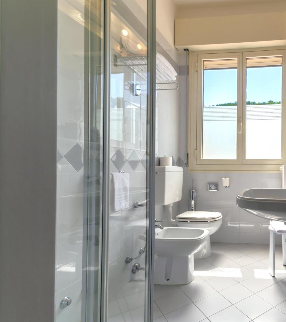 Bright bathroom with shower, sink, bidet, toilet, and large window.